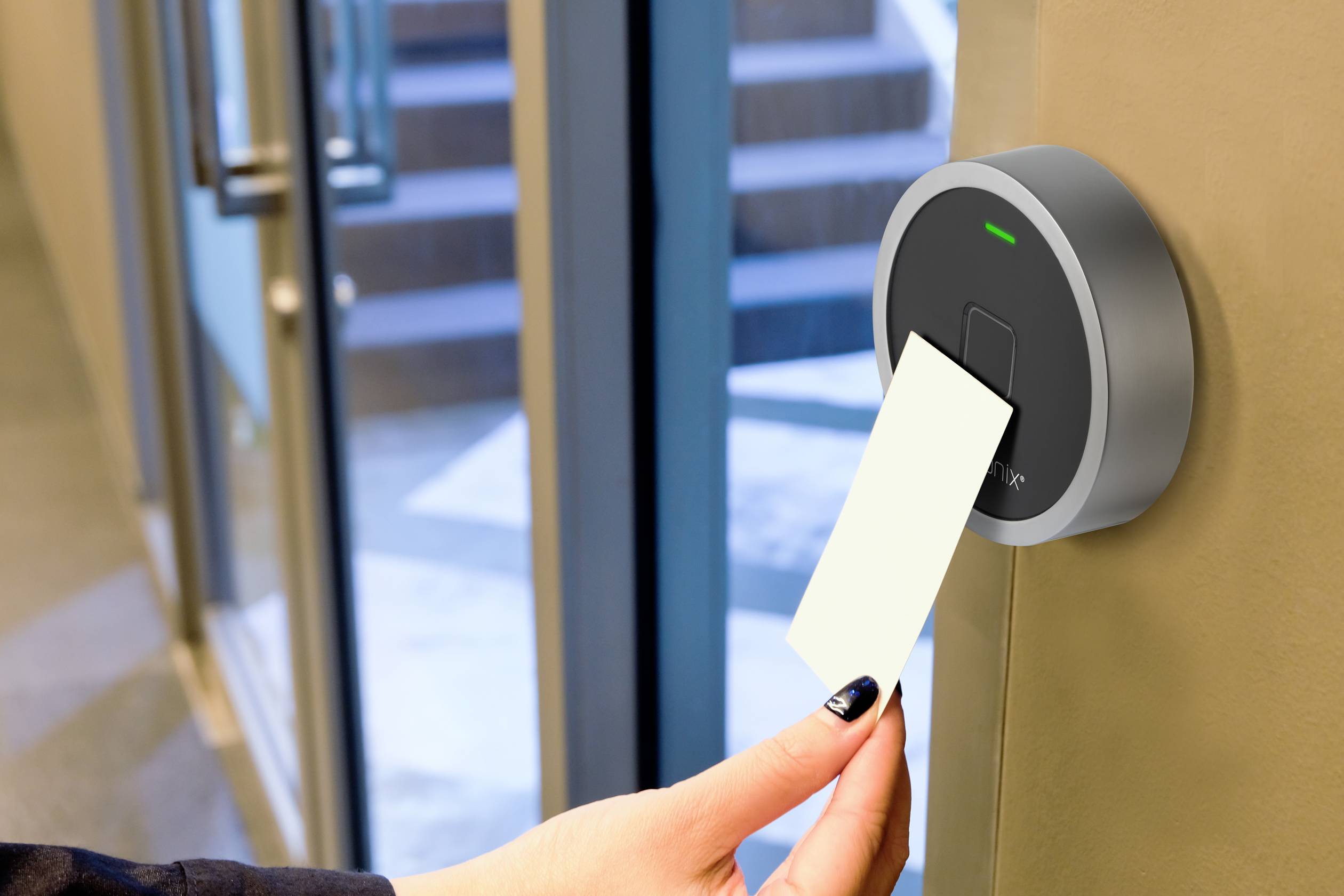 A hand holds an access card up to a modern card reader on a door to grant entry to a building.