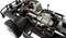 A remote-controlled car without bodywork reveals the electric motor, gearbox, and wiring of the front axle in intricate detail.