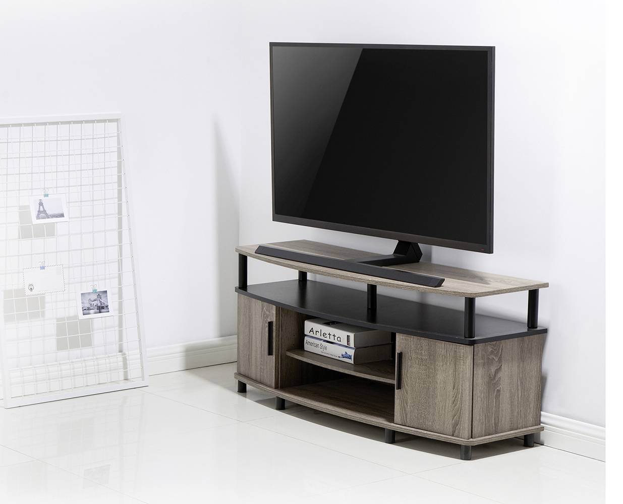A modern television set on a stylish, dark wooden TV stand in a bright room. A wire-frame decorative piece is positioned to the left.