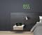 A modern bedroom with a digital clock on the wall displaying '18:55'. Next to it, a table lamp and a bed with grey bedding.