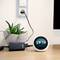 A round digital alarm clock displays the time as 17:18. Next to it sits a plant in a pot, and a charger is plugged in.