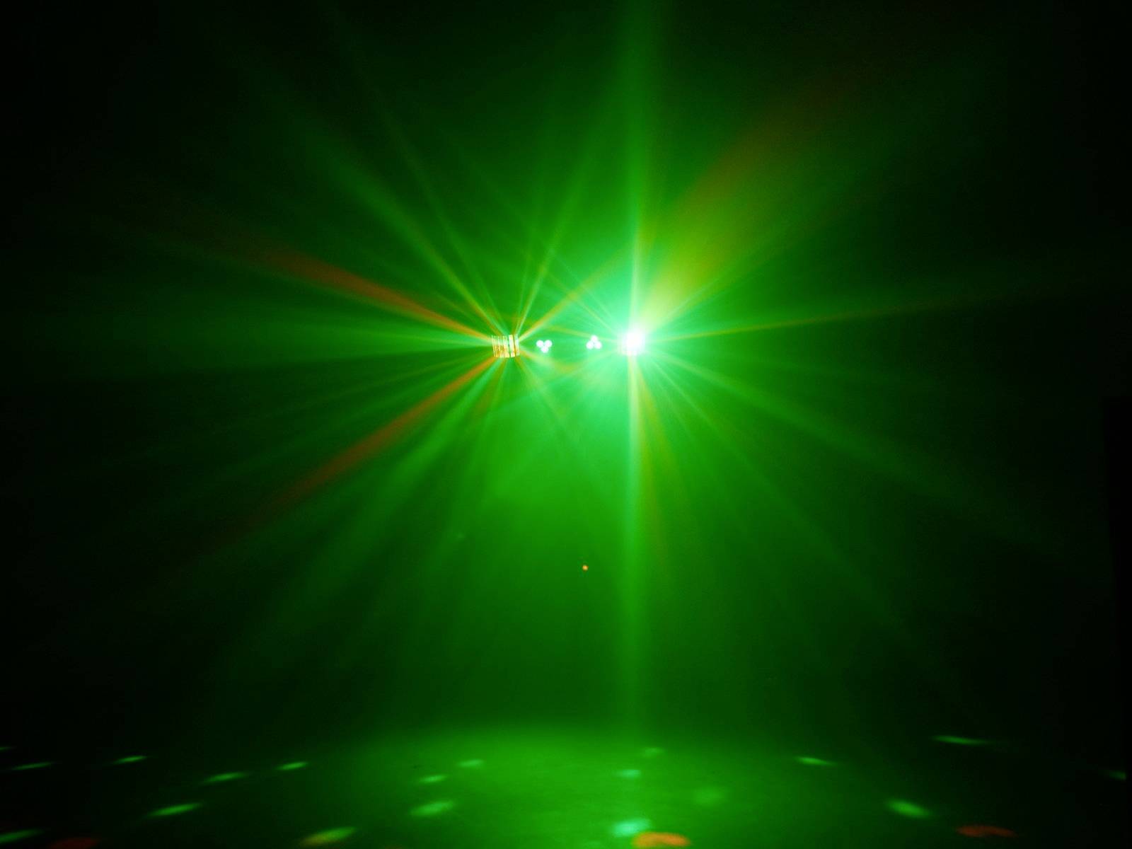 Green lights beam in the dark space, colourful light points on the floor create a vibrant disco atmosphere.