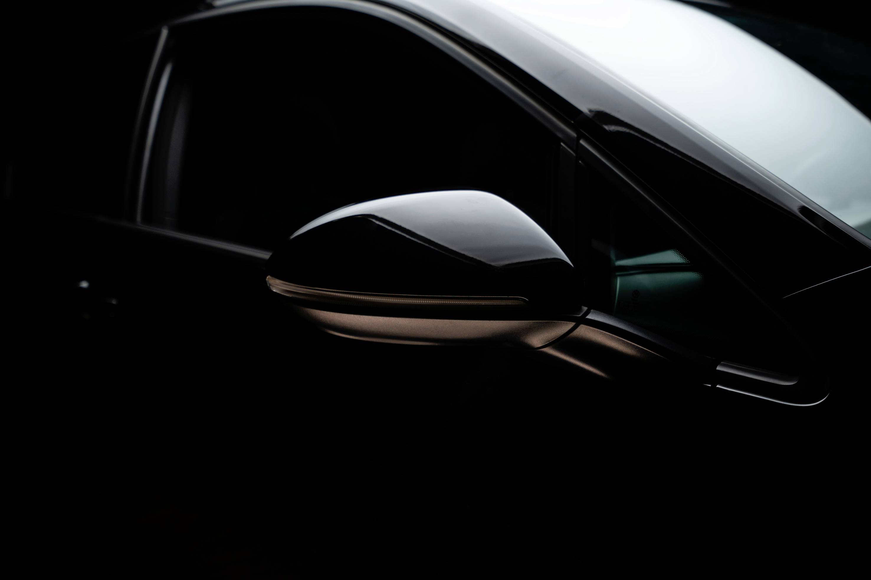 A gleaming, black car wing mirror highlighted against a dark background.