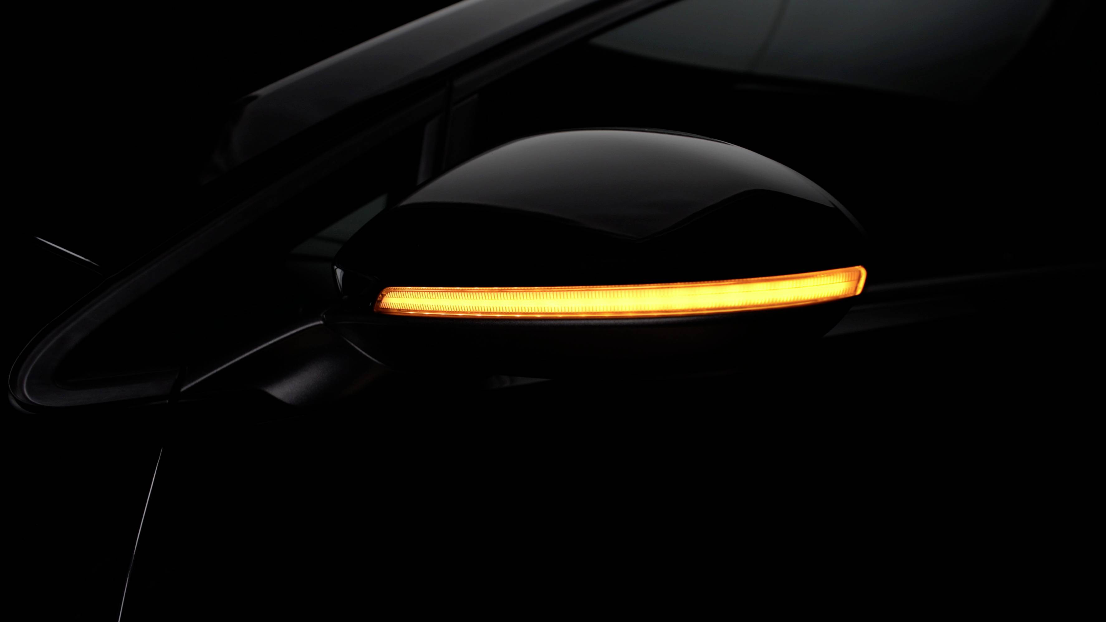 Car wing mirror with an activated yellow indicator light in a dark environment.