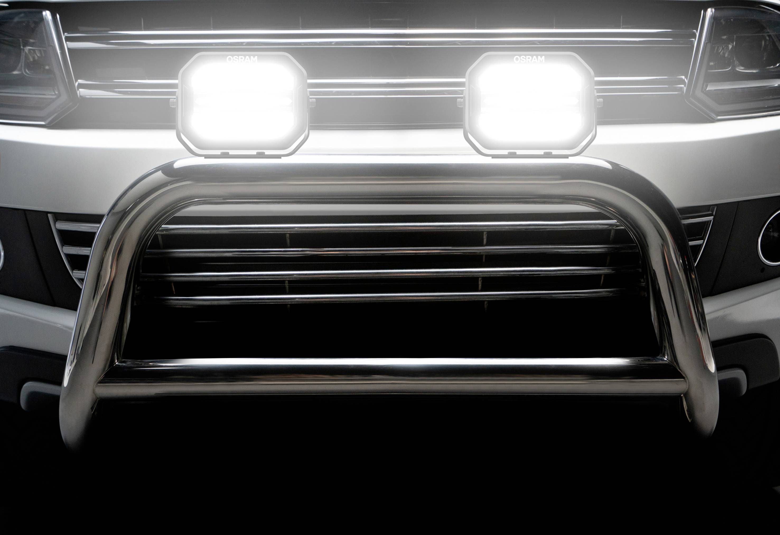 Close-up of a vehicle front with a chrome-plated bull bar and switched-on LED headlights.