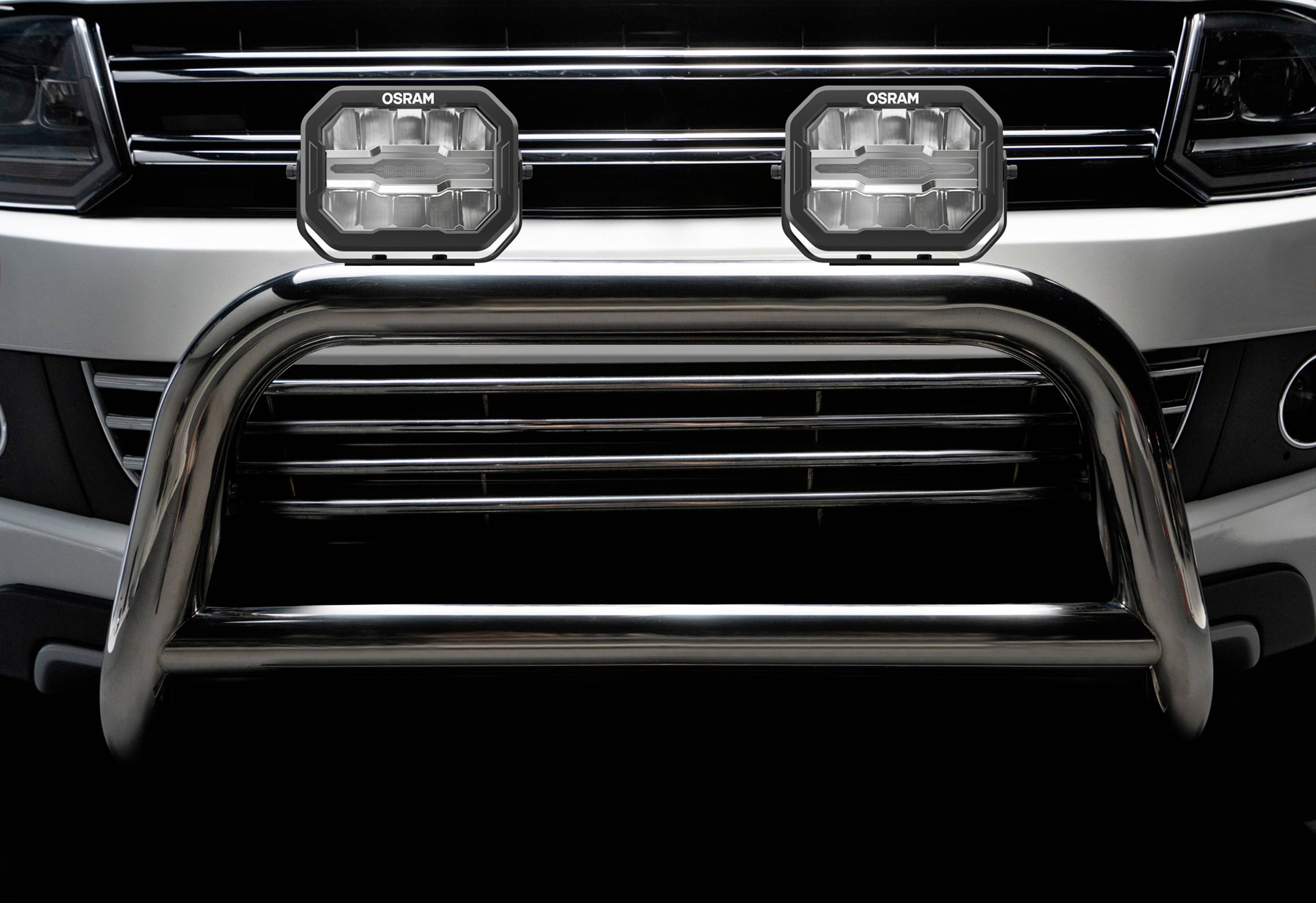 A close-up of a metal vehicle bumper with two mounted rectangular OSRAM headlamps.