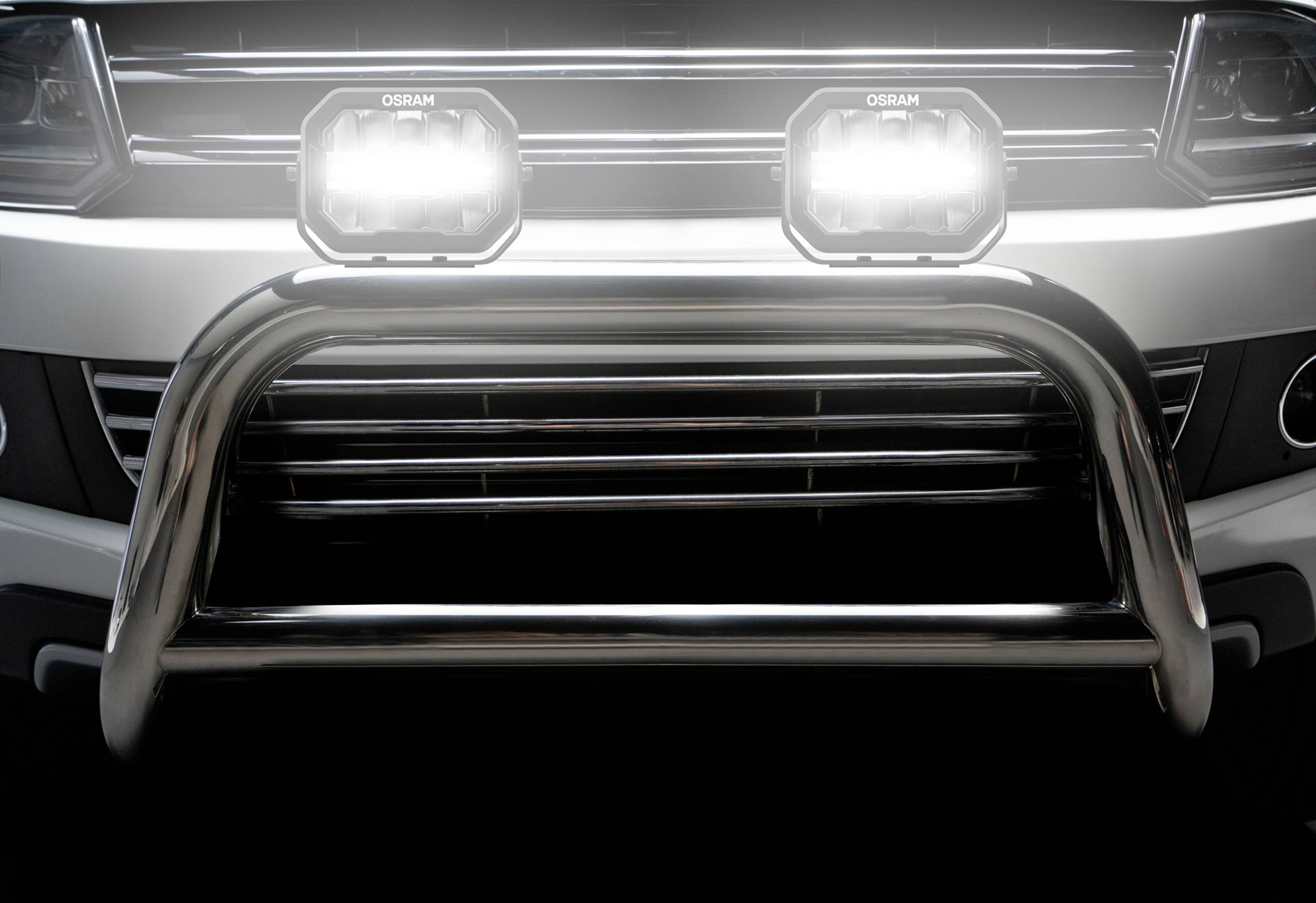 Close-up of a car with an additional protective bull bar and two illuminated headlamps at the front.