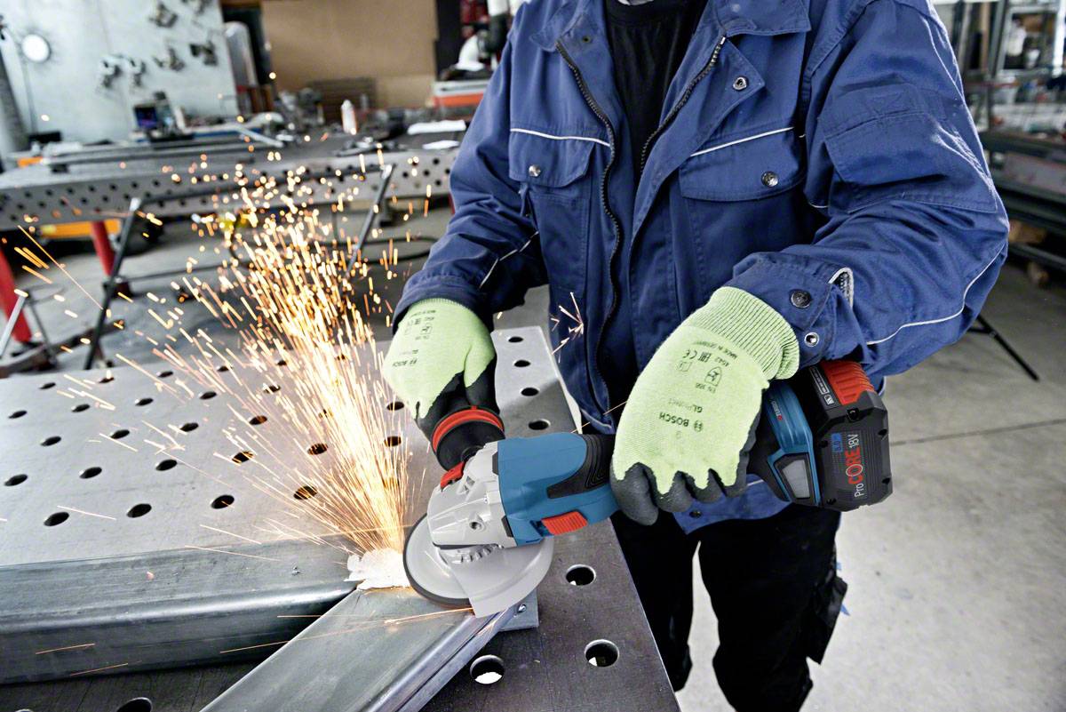 A person is grinding metal with an angle grinder, sparks flying. The person is wearing gloves and a blue work jacket.