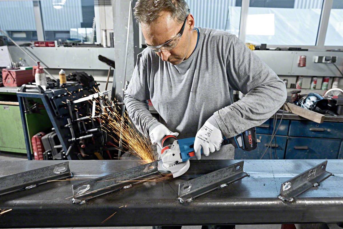 A man is cutting metal with an electric grinding machine in a workshop. Sparks are flying, safety equipment is being worn.