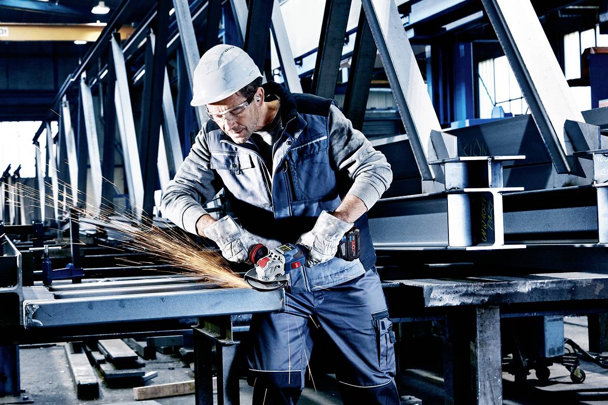 A worker in protective clothing grinds metal in a workshop, sparks flying from the grinding machine.