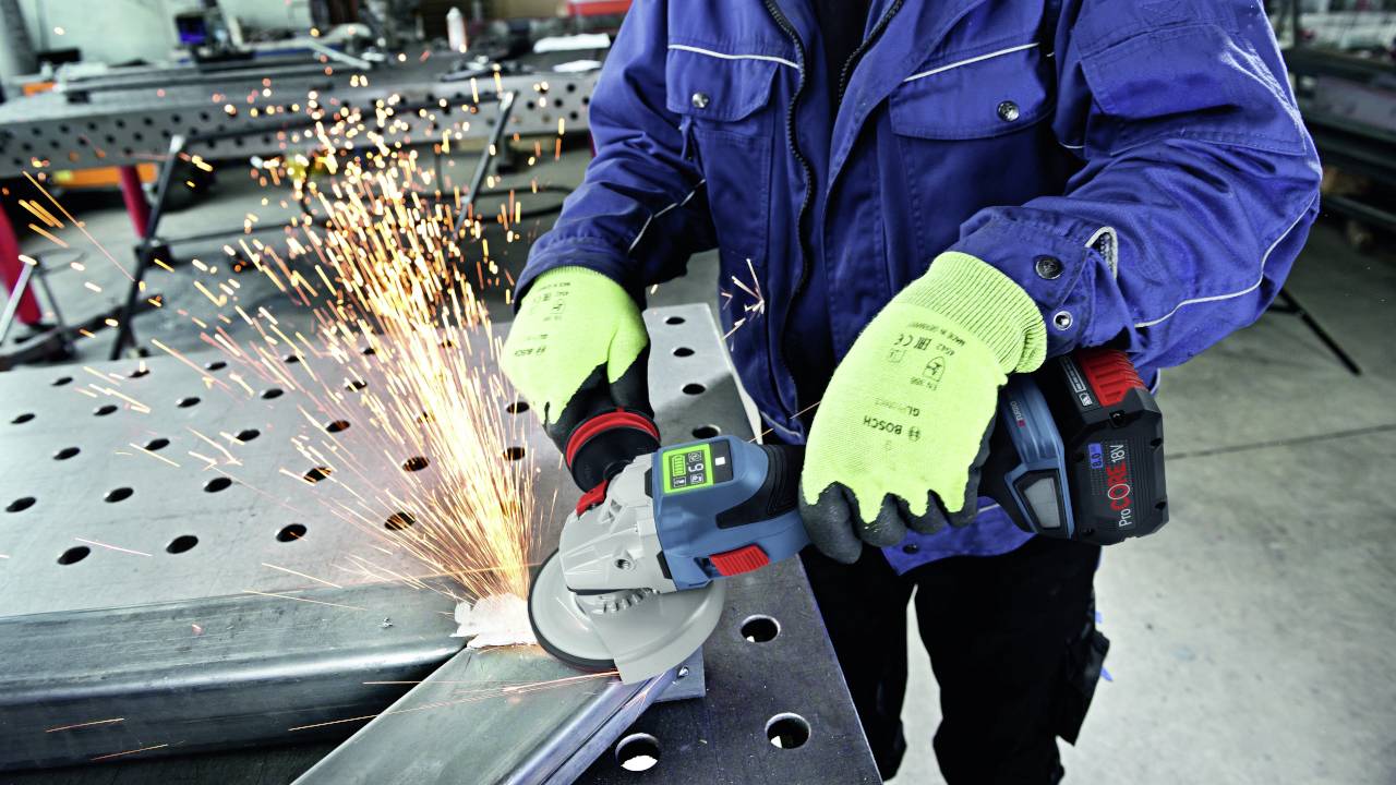 A person wearing protective equipment is grinding metal with an angle grinder, sparks flying.