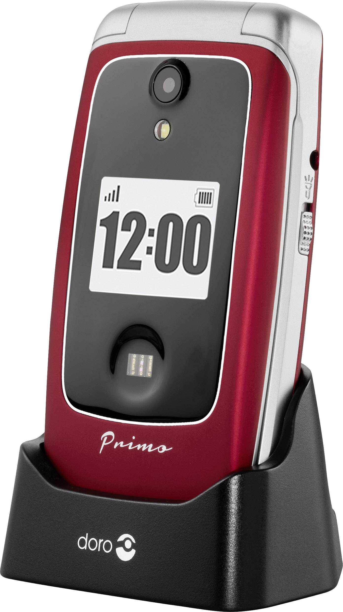 A flip mobile phone in a charging station with a black display showing '12:00'. The phone has a red back panel and a camera.