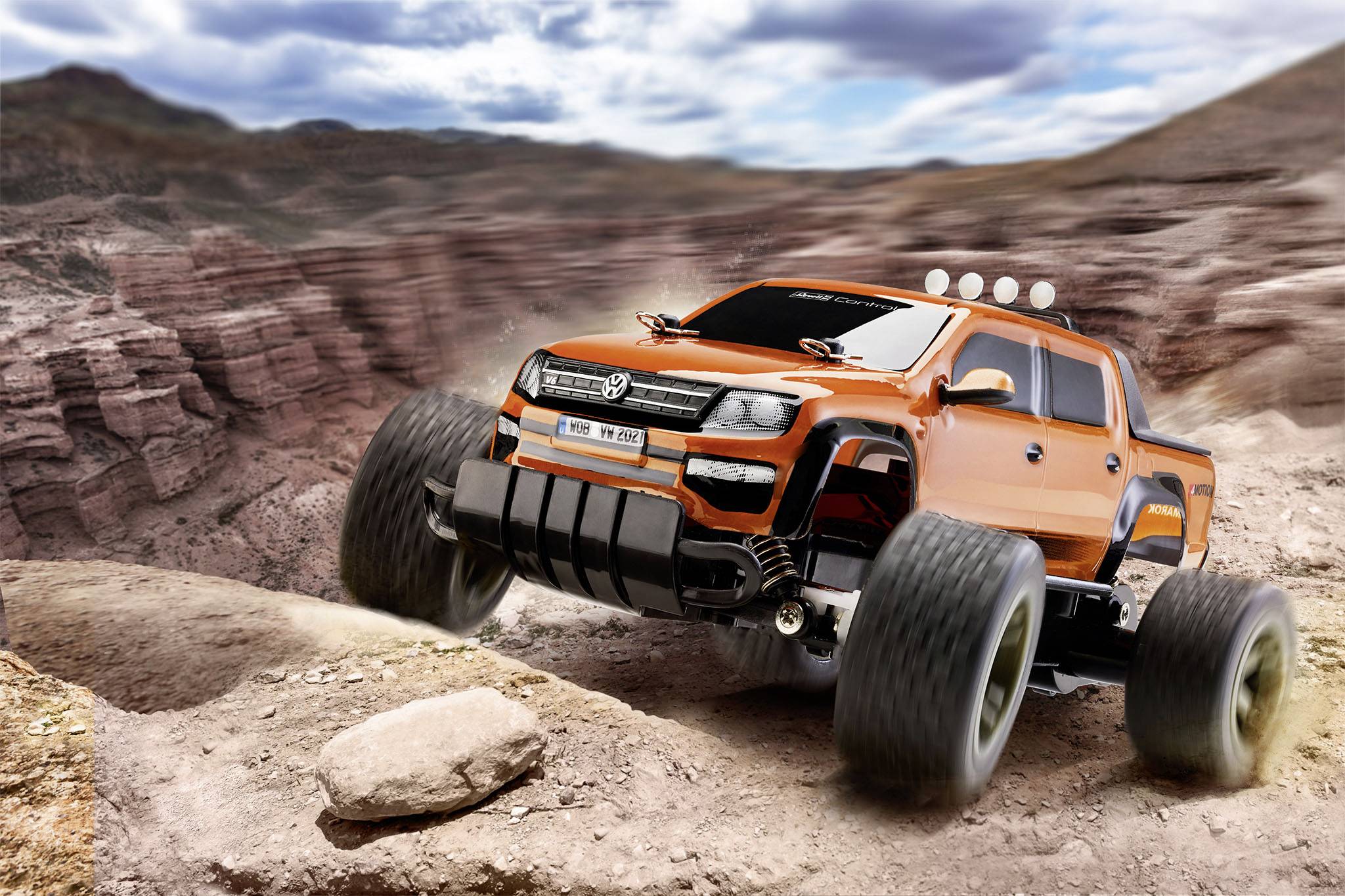 An orange, off-road truck drives across a rugged, rocky landscape. A dramatic sky looms in the background.