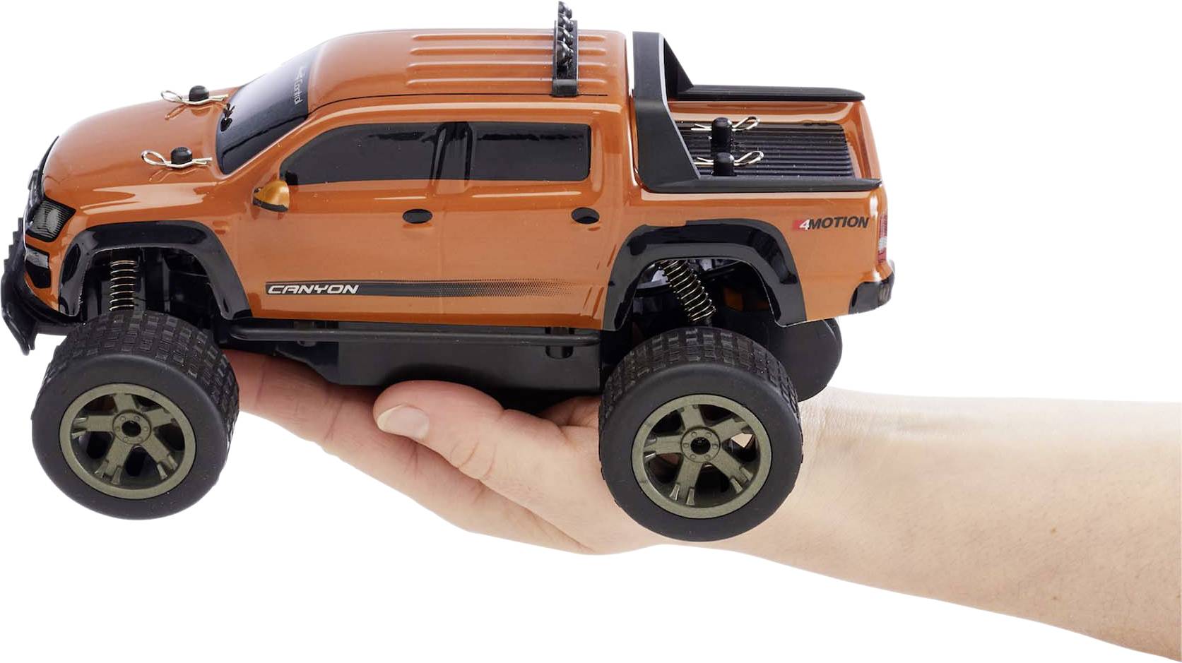 A person is holding a small, orange toy pick-up truck to scale, which looks like an off-road vehicle.