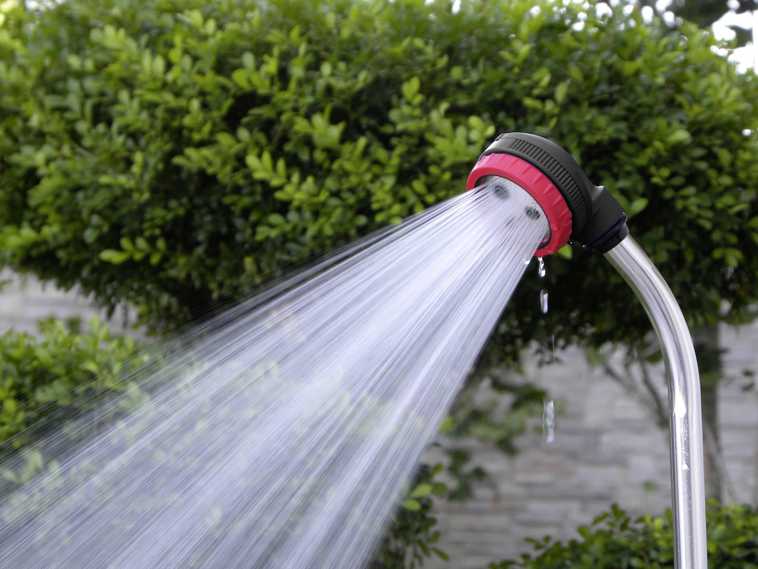 Outdoor shower with water spray, surrounded by green bushes.
