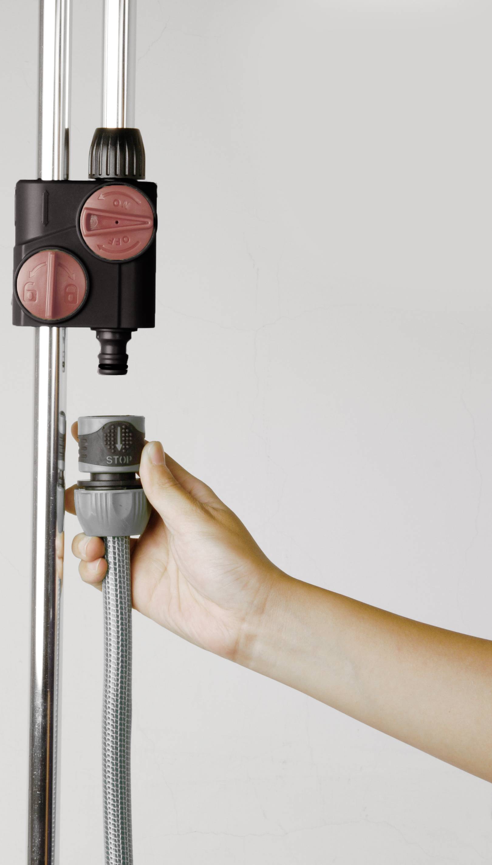 A hand connects a grey hose to a black valve on a vertical metal pole.