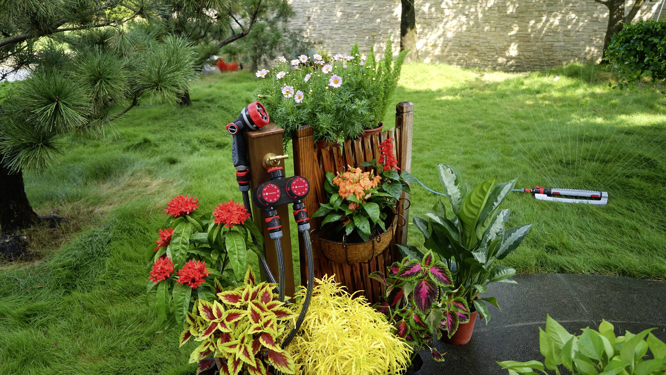 Garden with various colourful flowers and plants, decorated with a wooden barrel and gardening tools. Background of lawn and trees.