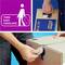 A person is carrying a carton labelled 'Tork Easy Handling'. The carton has integrated hand holes for easier carrying.