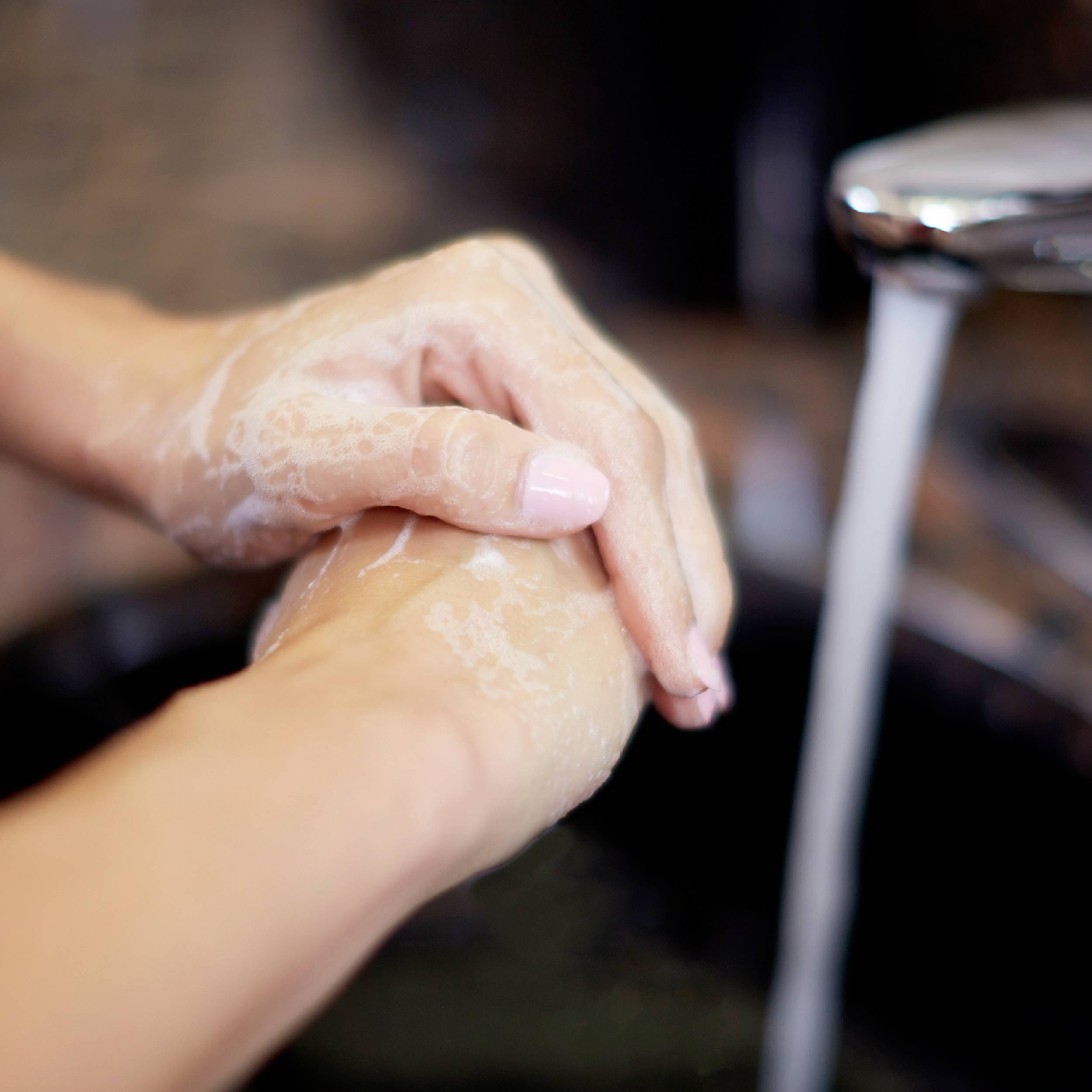 Hands being washed under a tap. Soap lathers on the skin. The image depicts hygiene practices of hand washing.