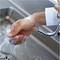 A person is washing their hands under running water in a stainless steel sink. Hands are lathered with soap.