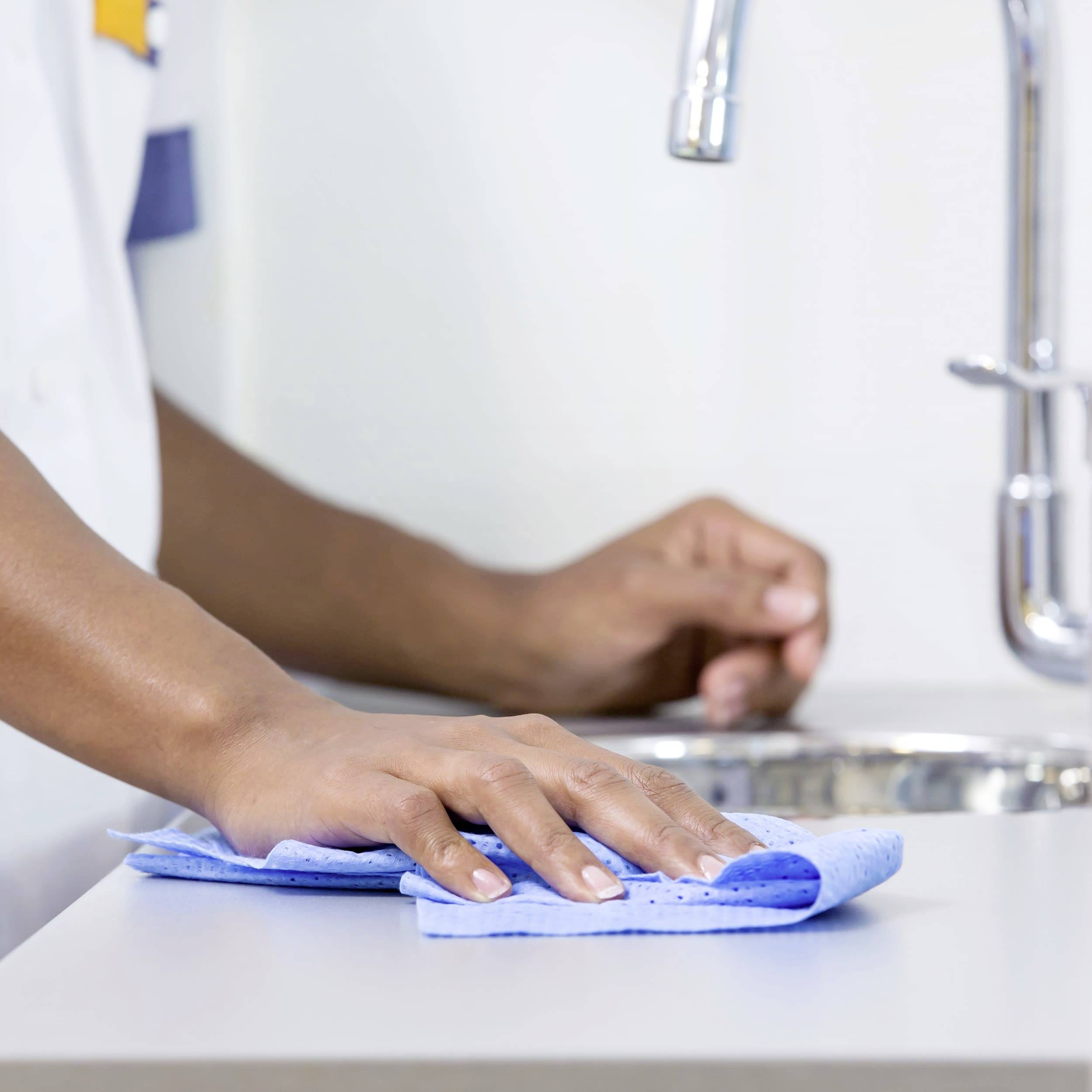 A person is cleaning the kitchen with a blue cloth next to a gleaming tap.