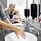 A woman is helping a small child wash their hands in a bathroom. Both are standing in front of a sink with a mirror.