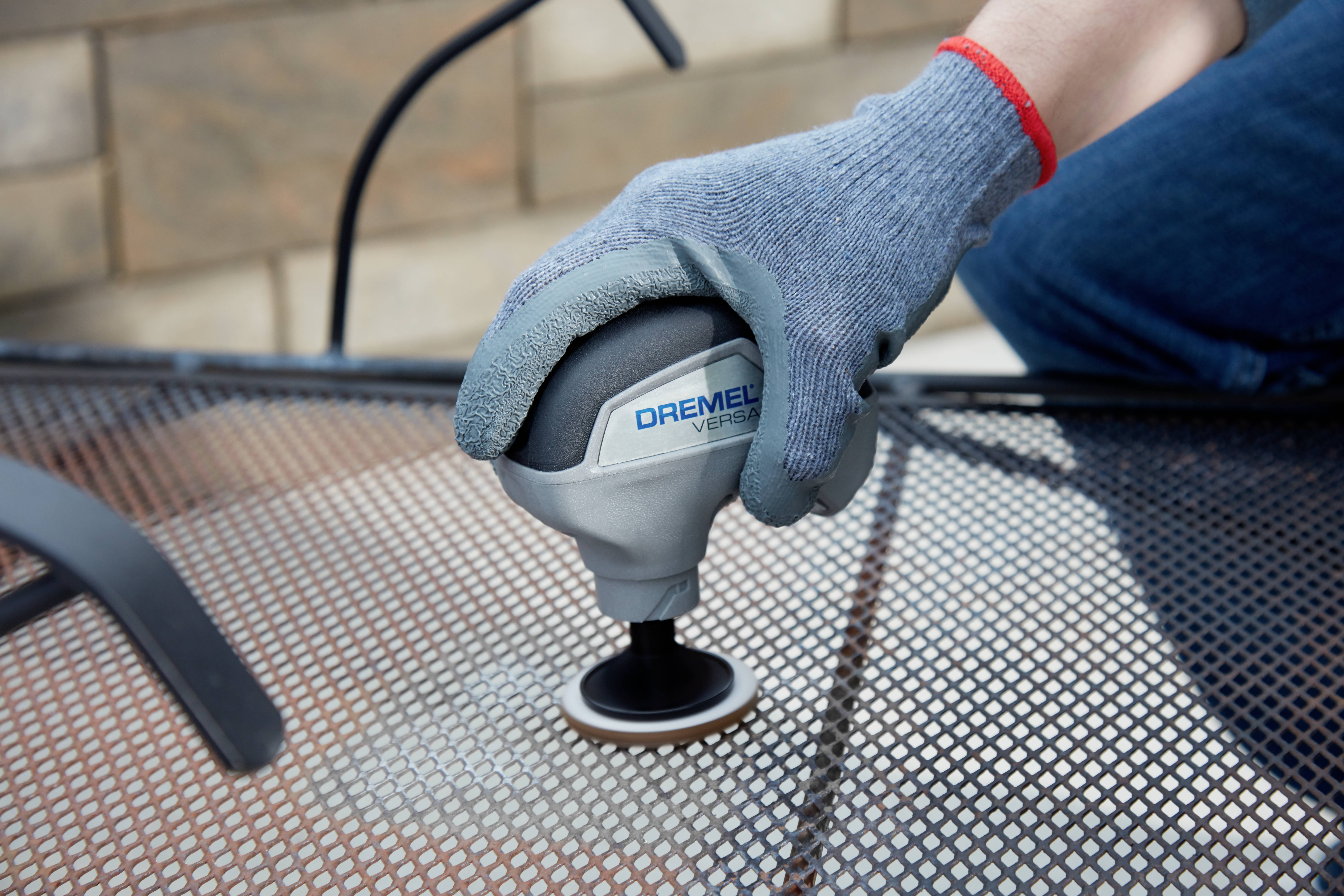 A person is grinding a metal surface with a Dremel tool. They are wearing grey gloves for protection.