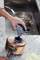 A person is using an electric cleaning device to polish a copper saucepan on a kitchen worktop. In the background, a pot is standing in the sink.