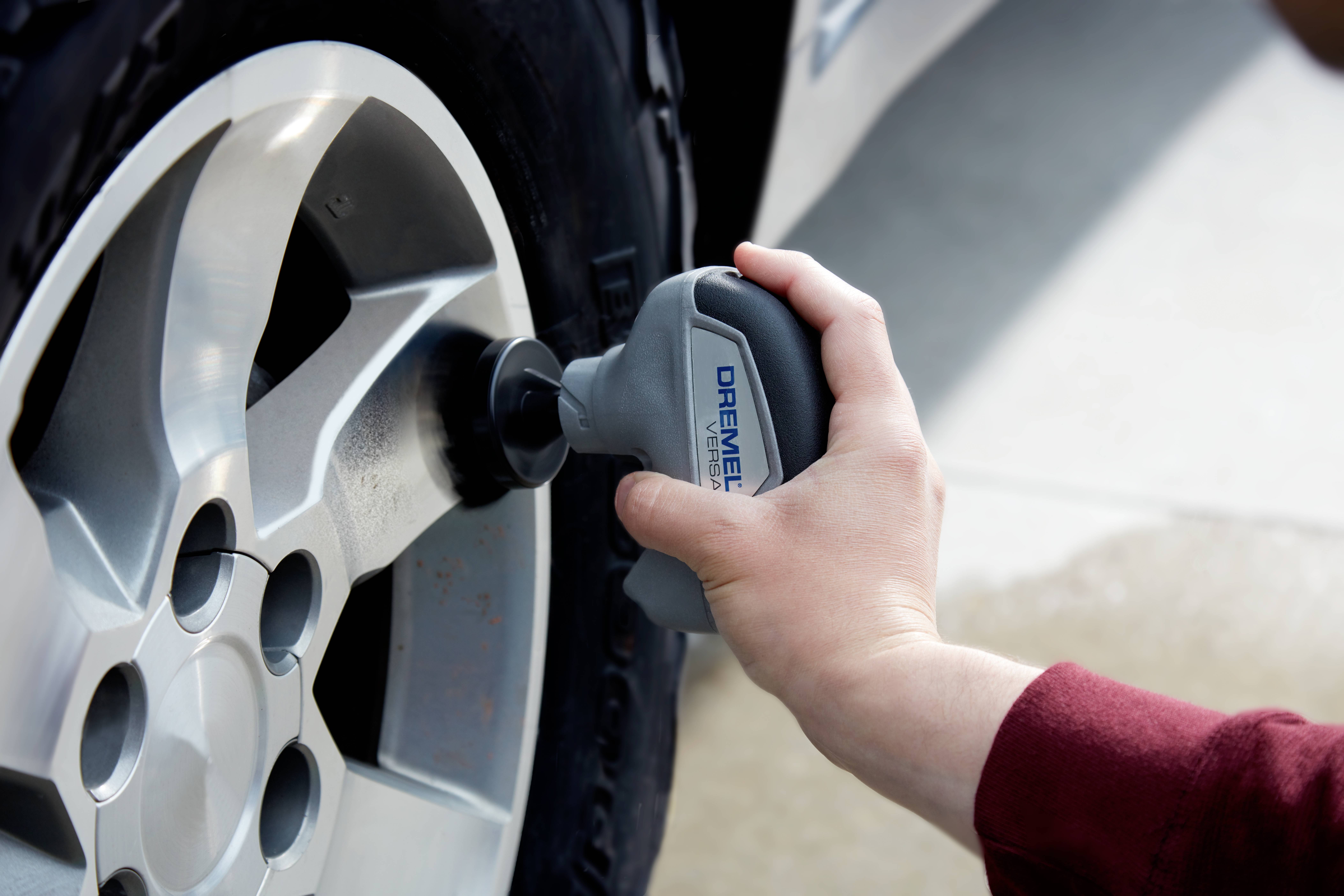 A hand holds an electric polishing device and is polishing a car wheel rim. The focus is on cleaning the rim.