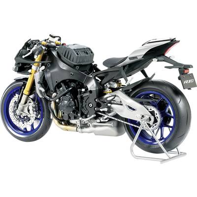 A sporty motorcycle without fairing, revealing its mechanics, with blue rims and a grey fuel tank, mounted on a stand.