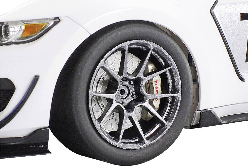 Close-up of a racing car tyre on a white racing car with silver alloy wheels and visible brake disc. Motorsport context.
