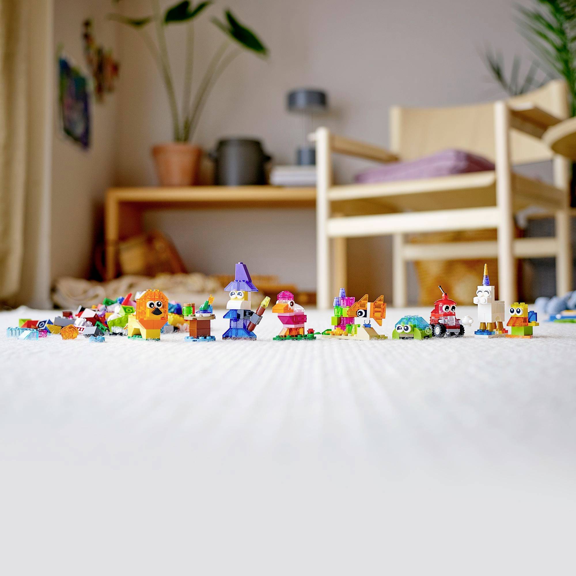 A row of colourful toy figures made from building blocks on a light-coloured carpet in a children's bedroom with a plant and chair in the background.