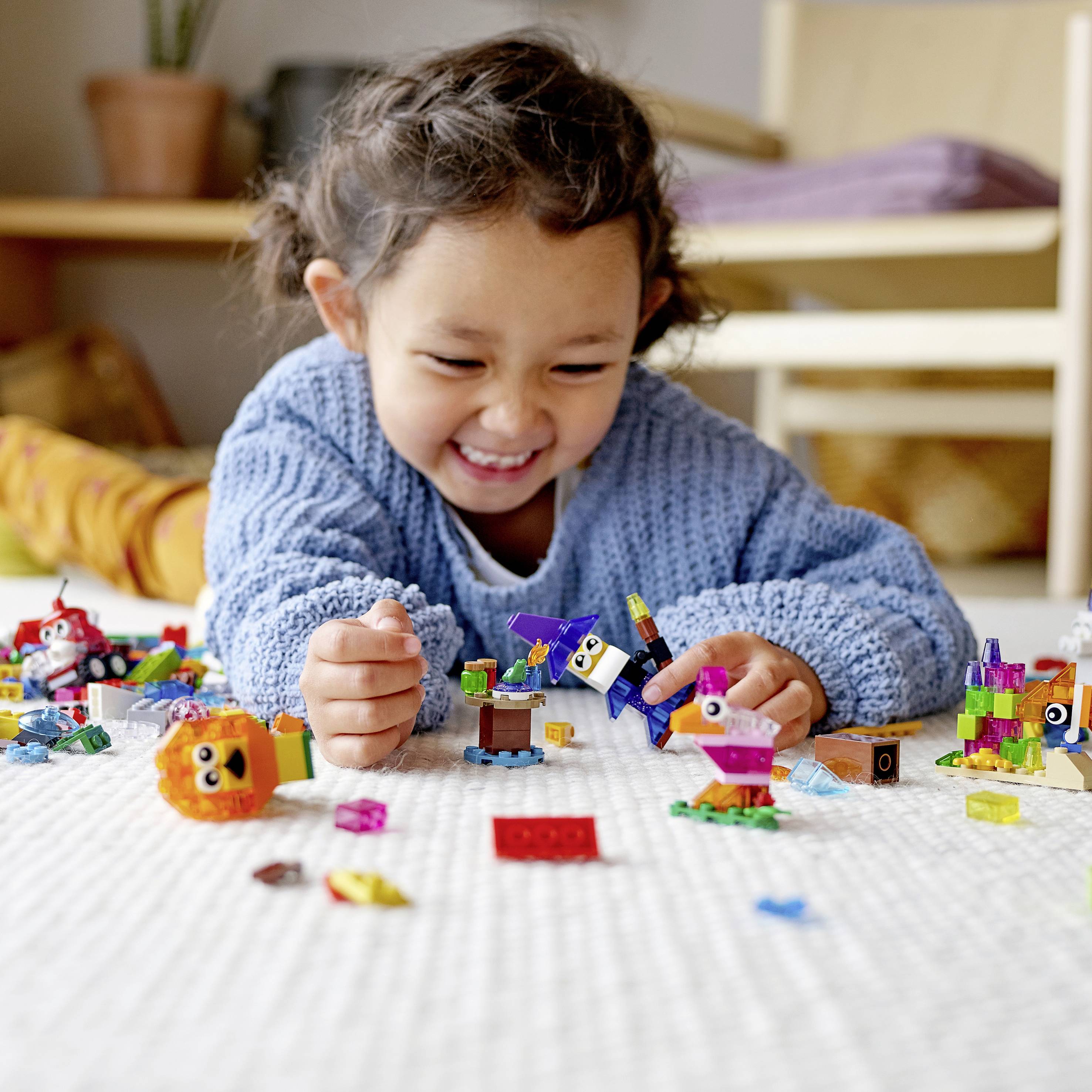 A laughing child in a blue jumper is playing on a carpet with colourful building blocks and enjoying creating figures.