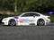 Racing car with white bodywork design, GT2 inscription, driving on asphalt. Background blurry and green.
