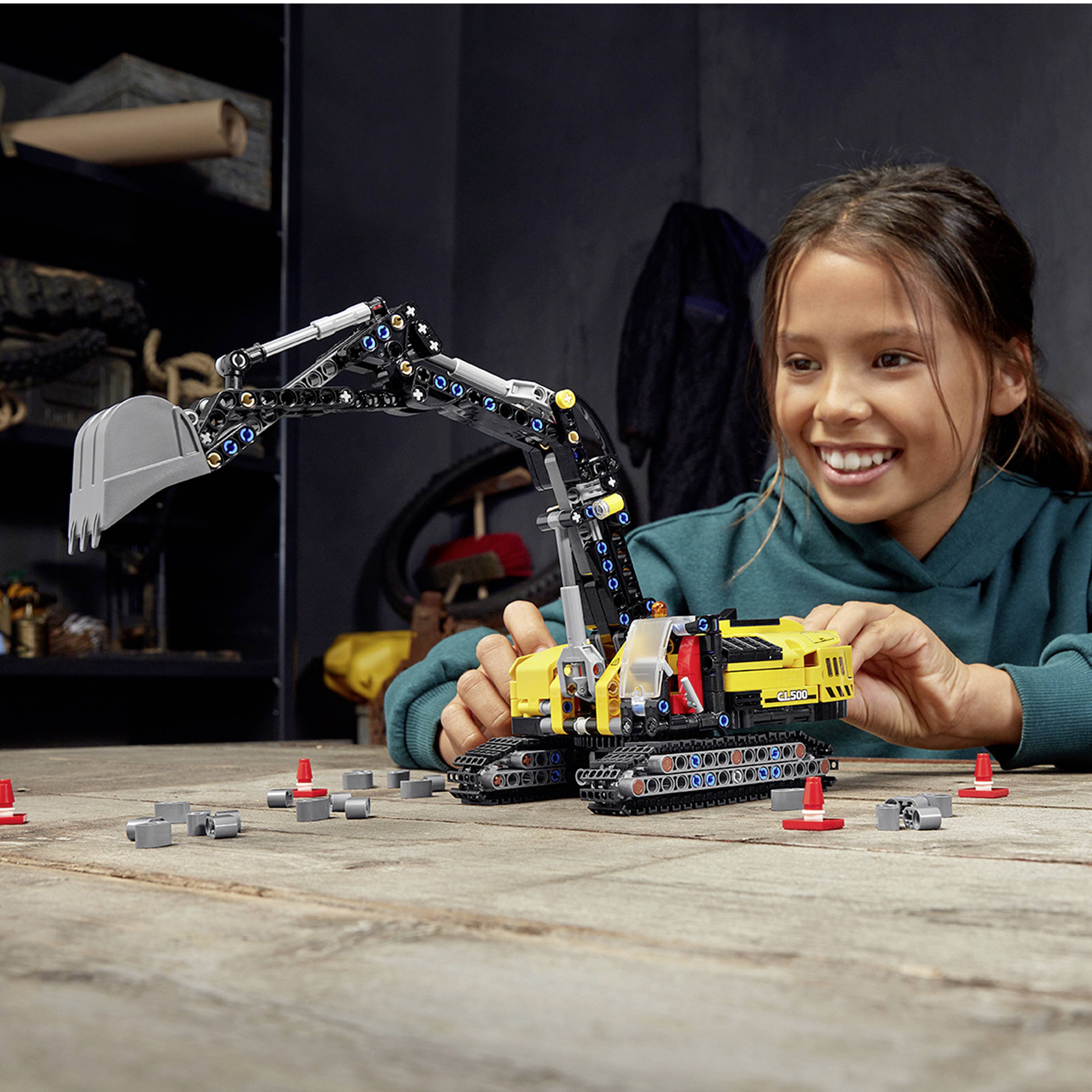 A girl is playing with a construction kit excavator on a table. She is smiling and looking concentratedly at the toy.