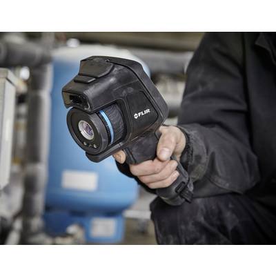A person is holding a FLIR thermal imaging camera, surrounded by technical equipment.