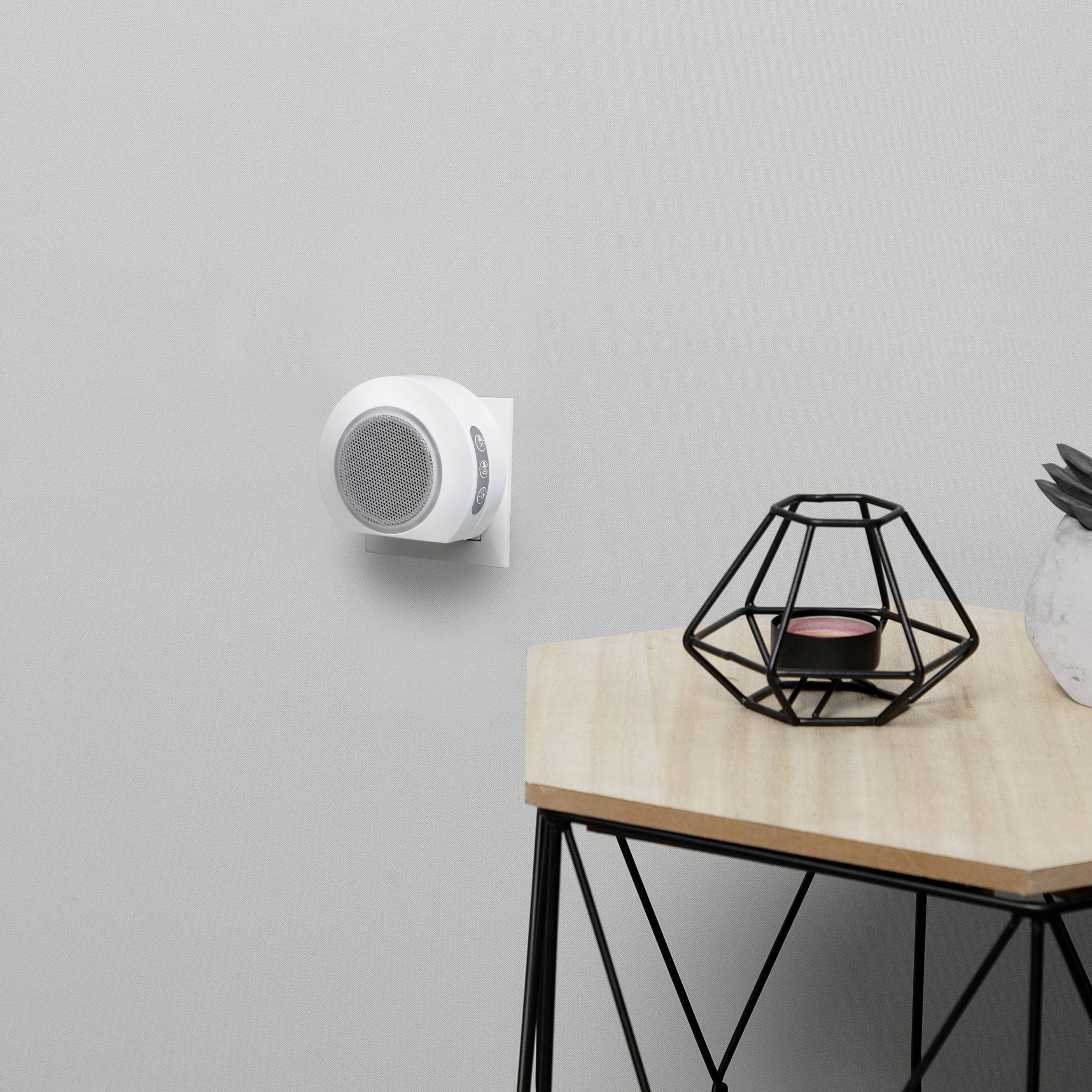 An air purifier plug-in in a white wall socket, next to a wooden table with a black geometric candleholder.