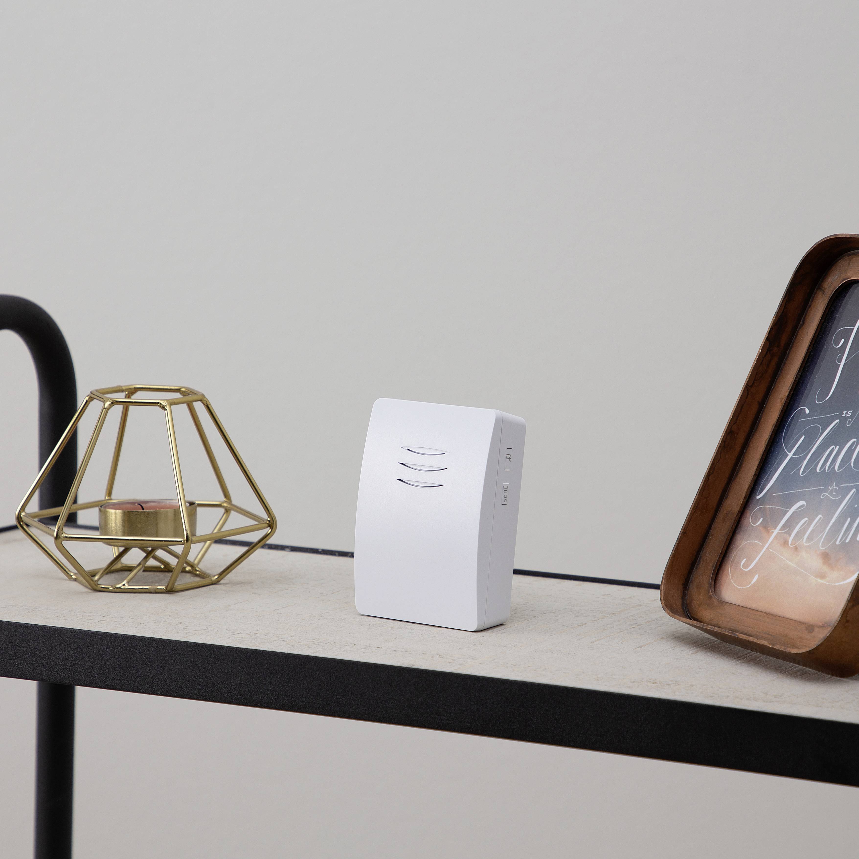 On a white shelf sits a small white air purifier next to a copper-coloured candlestick and a framed picture.