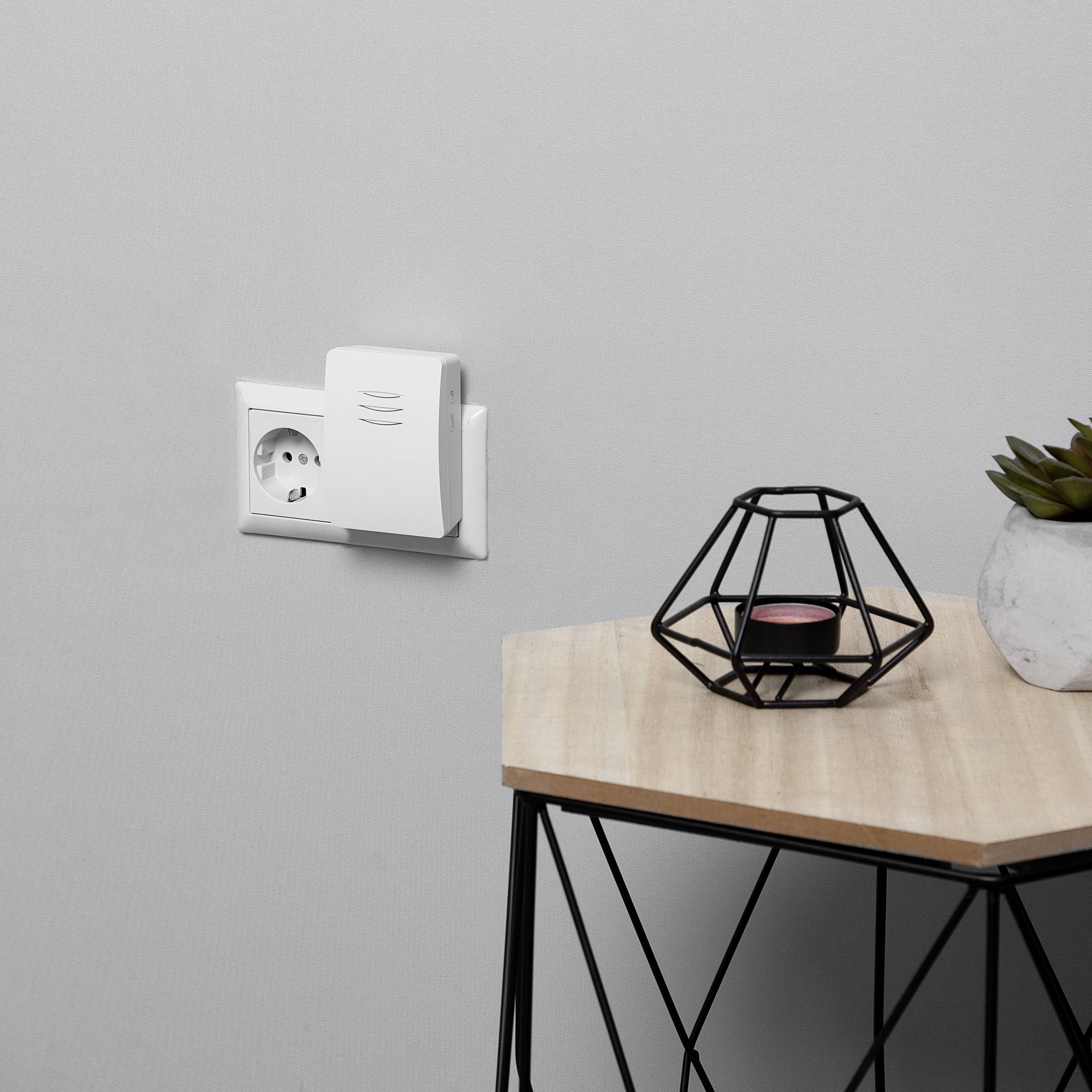 A white socket with an insert in a grey wall; beside it a table with a modern candle holder decoration.