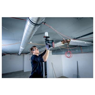 A person wearing safety goggles uses a power tool to install piping in a ceiling, surrounded by electrical wires in an unfinished room.