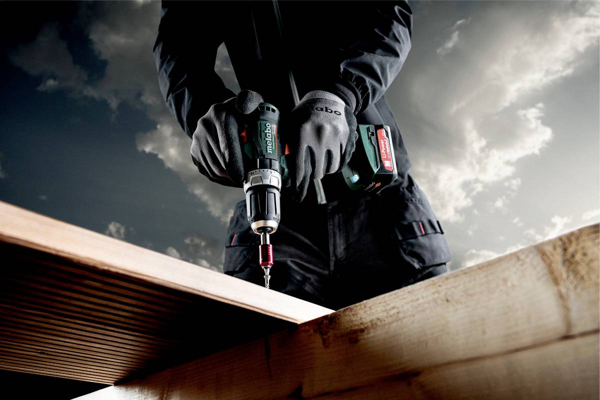 A person is using a cordless drill to connect wooden planks; dark clouds in the sky in the background.
