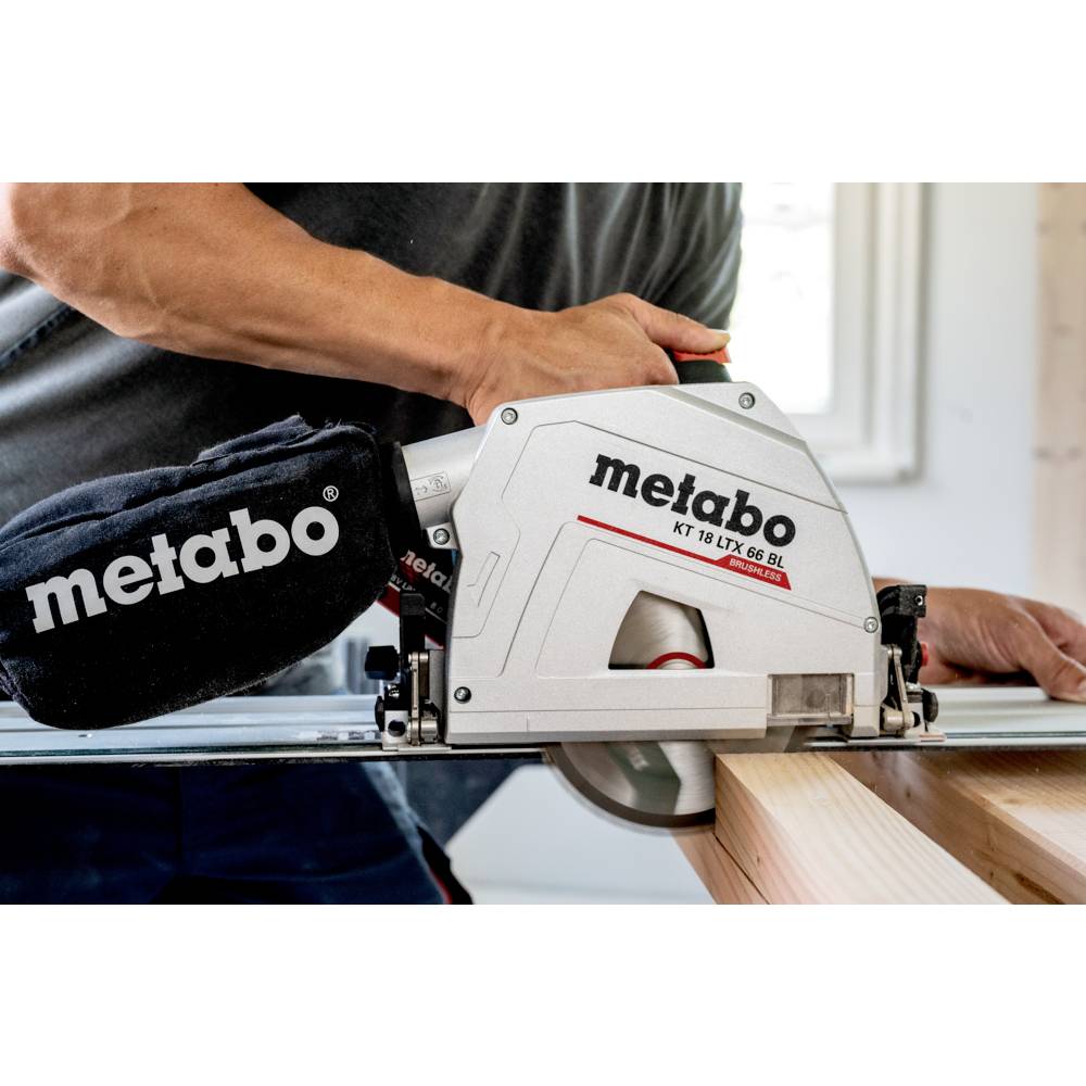 A person uses a Metabo circular saw on a wooden plank indoors, focusing on precision cutting. The saw is cordless with an attached dust bag.