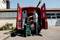 A man is unloading tools from a red delivery van. He is stacking green crates on a trolley in front of a garage.