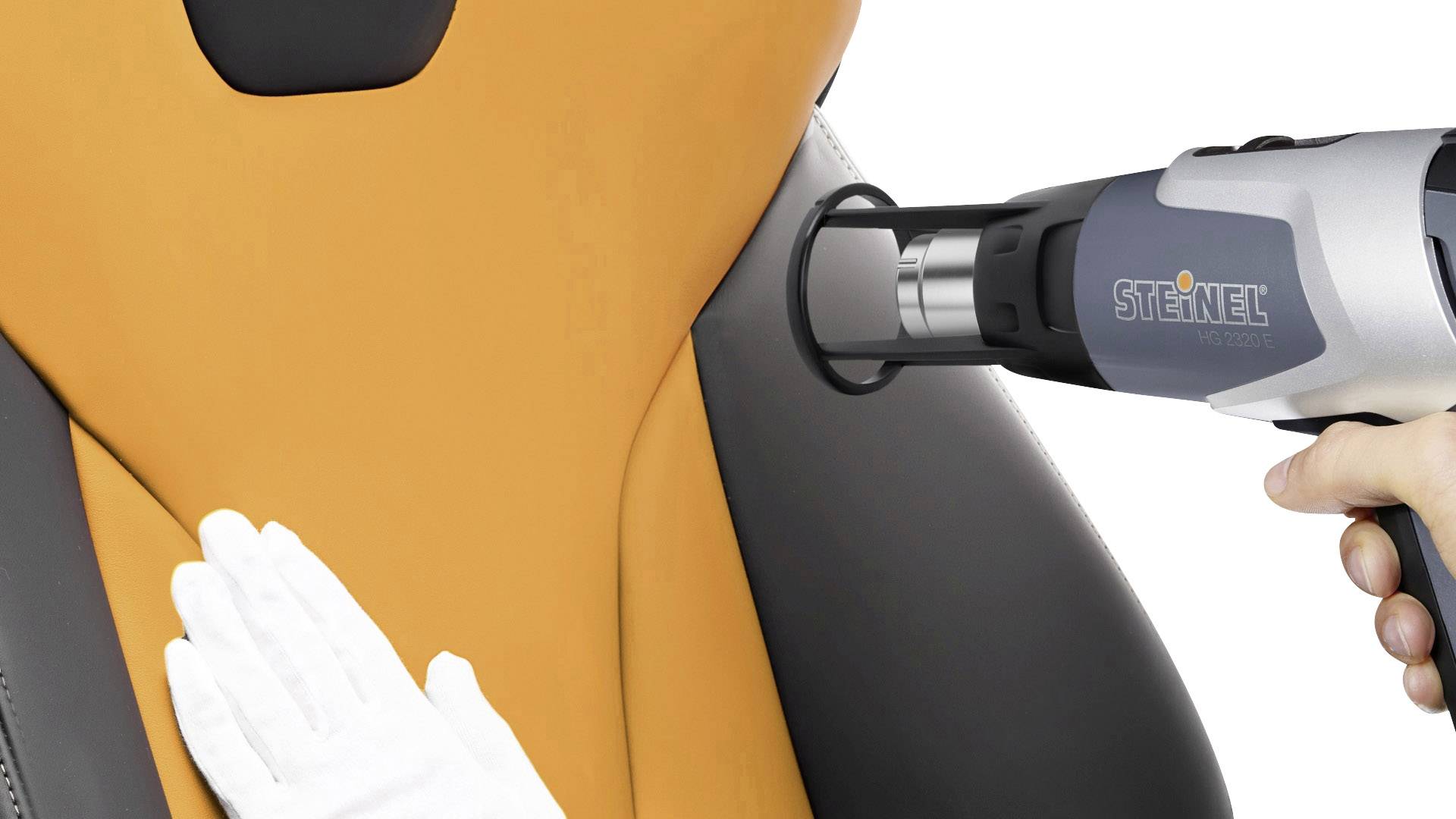 A person is working on an orange-black car seat with a hot air dryer. In their other hand, they are holding a white glove.
