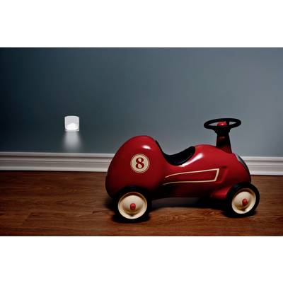 A red toy car with the number 8 sits on a wooden floor in front of a blue wall. In the background, a night light glows.