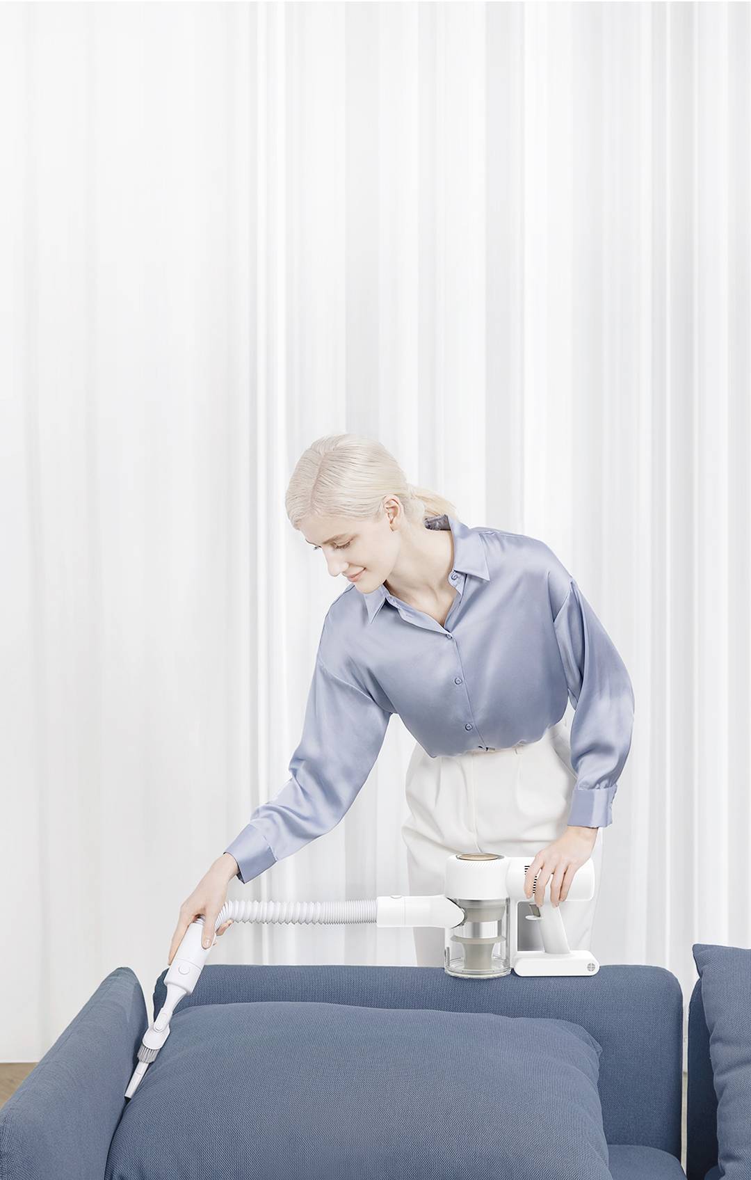 A person is using a vacuum cleaner to clean a blue sofa.<br><br>Note: This is a direct translation to British English. The sentence structure and vocabulary are already quite neutral and international, so minimal changes were needed.