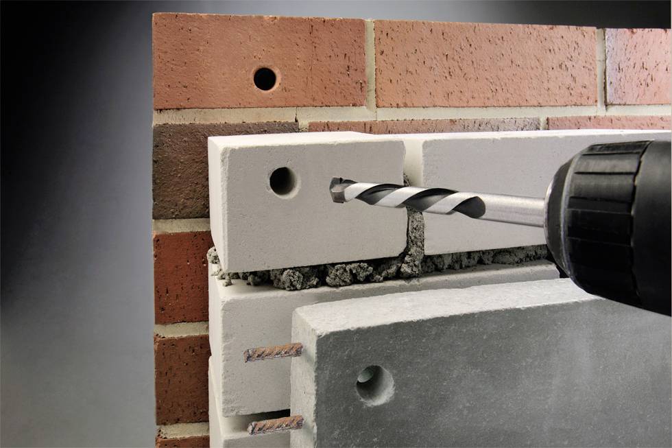 A drill penetrates a brick wall to create an opening in a hollow brick.