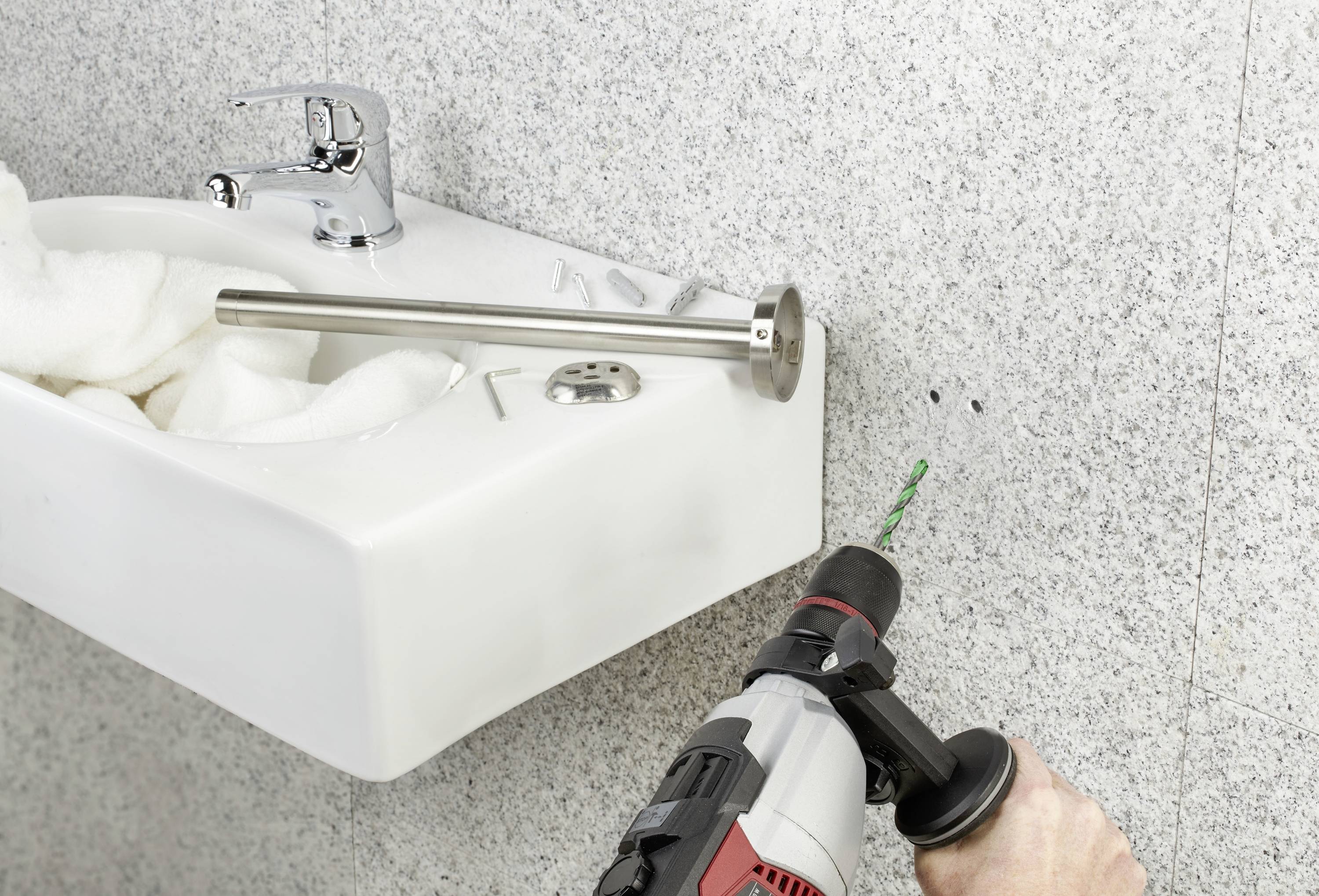 A person is drilling into a wall next to a white sink. Preparing to install a grab handle.