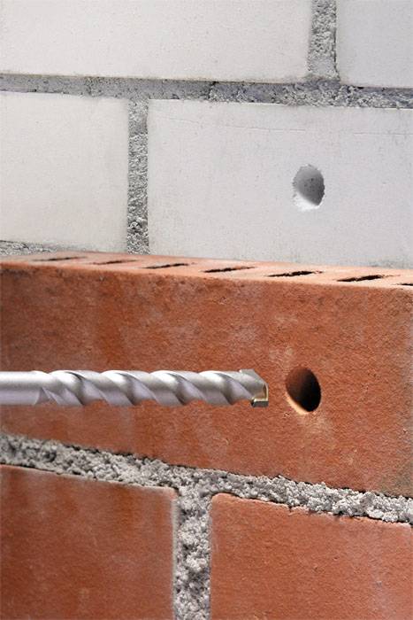 'A drill against a red brick wall with a drilled hole.'