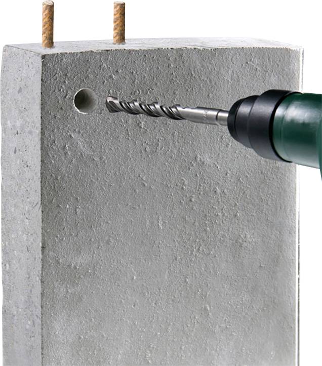 A drill is boring a hole into a concrete block. Two reinforcement bars are visible at the top.
